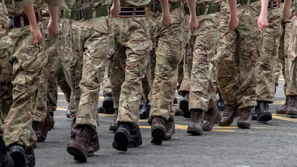 A number of soldiers in camouflage uniform marching together. They are wearing black boots and are marching in sequence.