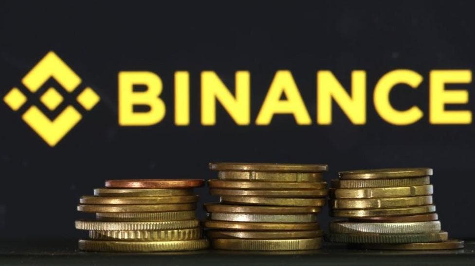 In this photo illustration, the Binance logo is displayed on a screen behind a stack of gold coins.