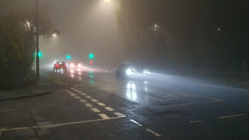 Foggy road with cars driving along - just seen their headlights