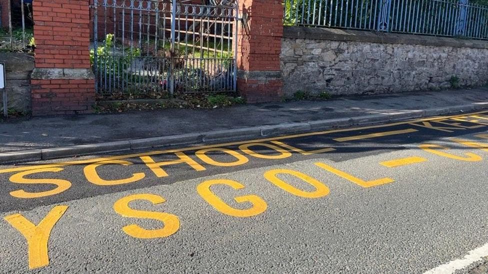 Brightly painted writing on the floor that says school in English and Welsh in yellow.