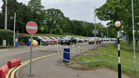A full car park with a stop sign and gate blocking the road. Trees and grass are on each side of the road
