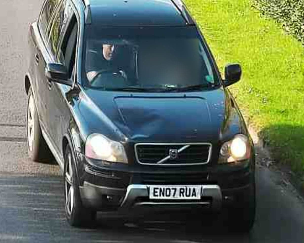 Simon Richardson drives a black SUV with headlights on along a road beside grass