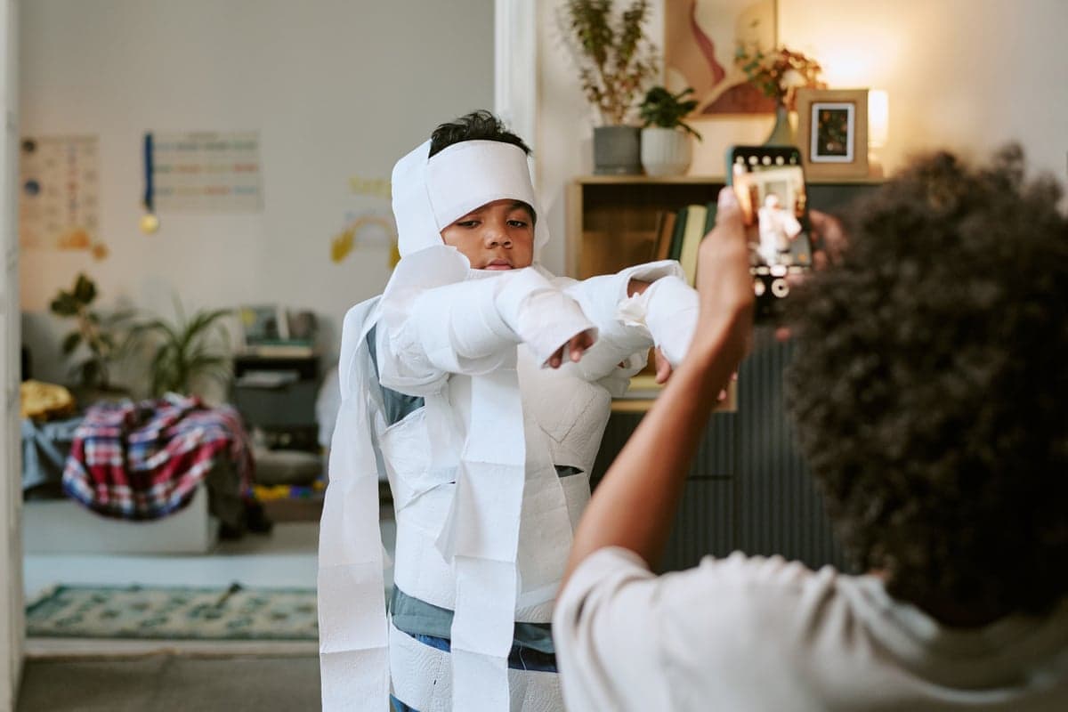 A boy stands wrapped in toilet paper as he has his photograph taken