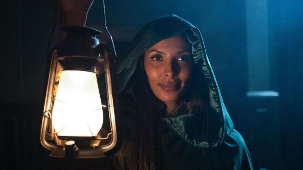 Maya Jama wearing a green cloak and holding up a lit lantern on the Celebrity Traitors.