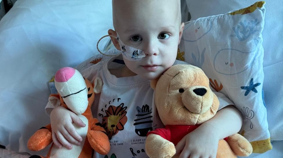 A little boy sat in a hospital bed with a soft toy of Tigger and Winnie the Pooh.